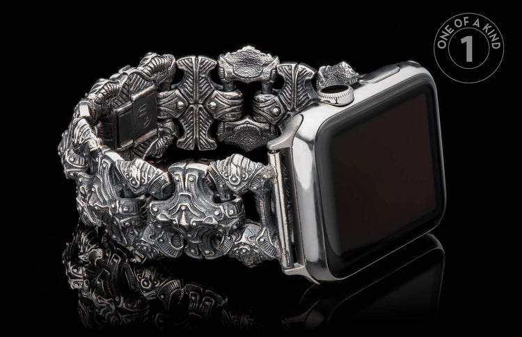 Ornate carved metal watch band with intricate links and a darkened silver finish, attached to a silver smartwatch.