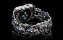 Ornate, sculpted dark silver metal watch band with intricate patterns and a red gemstone, attached to a smartwatch.