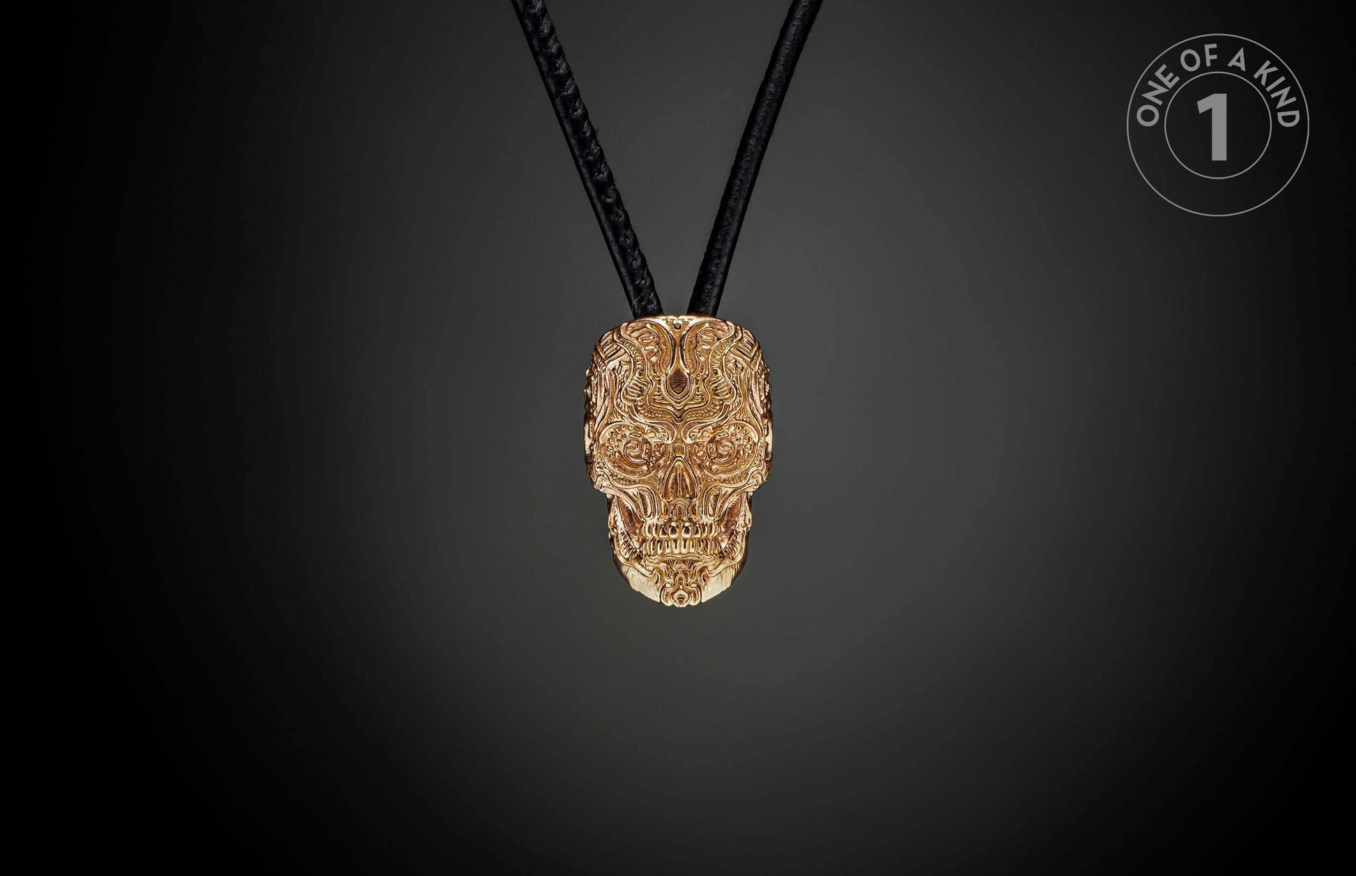 Golden skull pendant with intricate relief patterns, hanging from black cords, and a 'ONE OF A KIND' label.