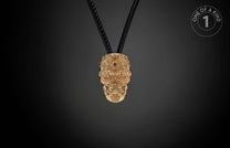 Golden skull pendant with intricate relief patterns, hanging from black cords, and a 'ONE OF A KIND' label.