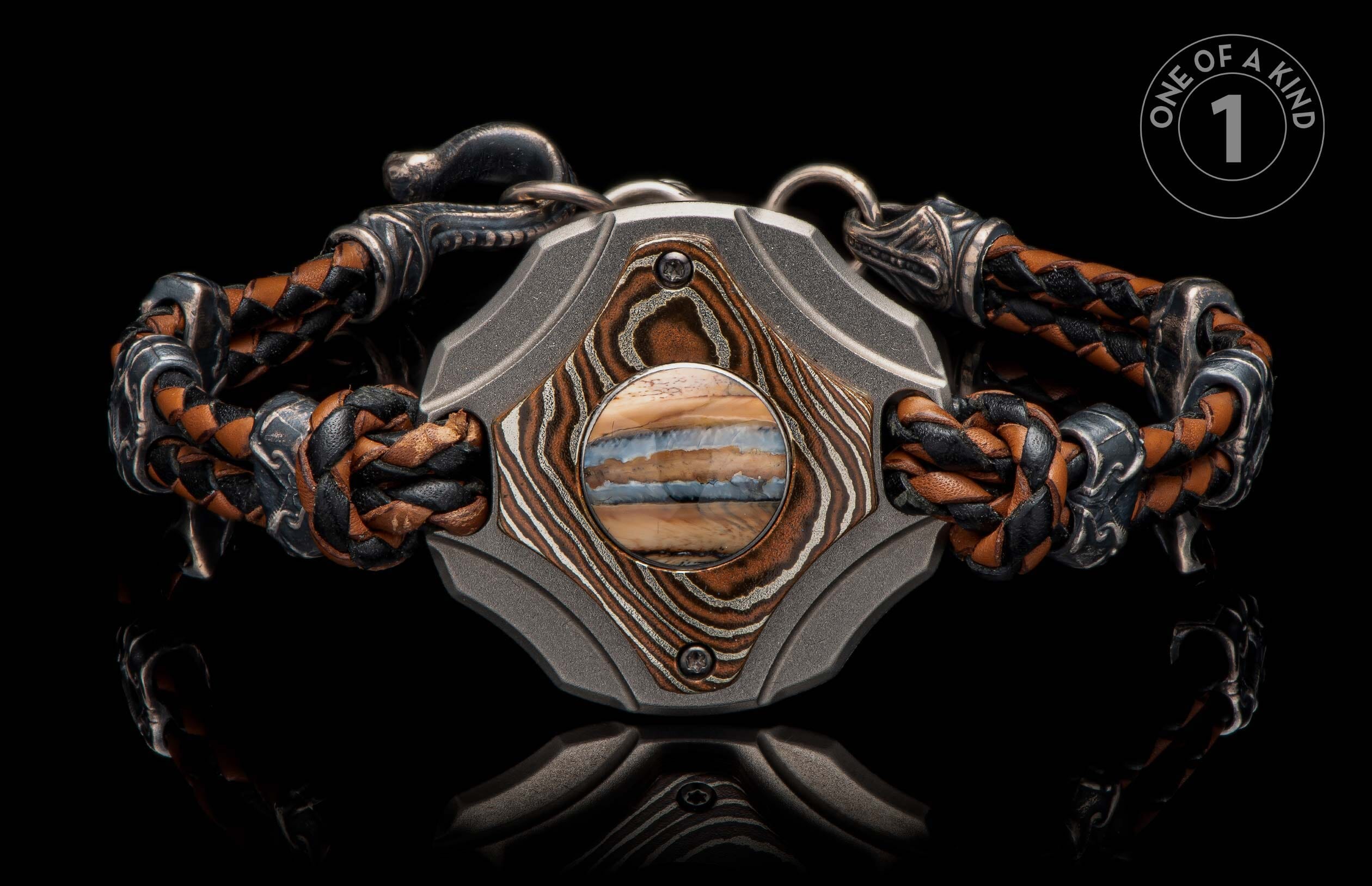 Braided brown and black leather bracelet with a dark metal center, featuring patterned copper-toned accents and a horizontally striped stone.