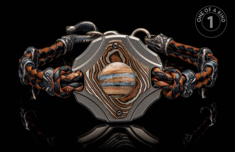 Braided brown and black leather bracelet with a dark metal center, featuring patterned copper-toned accents and a horizontally striped stone.