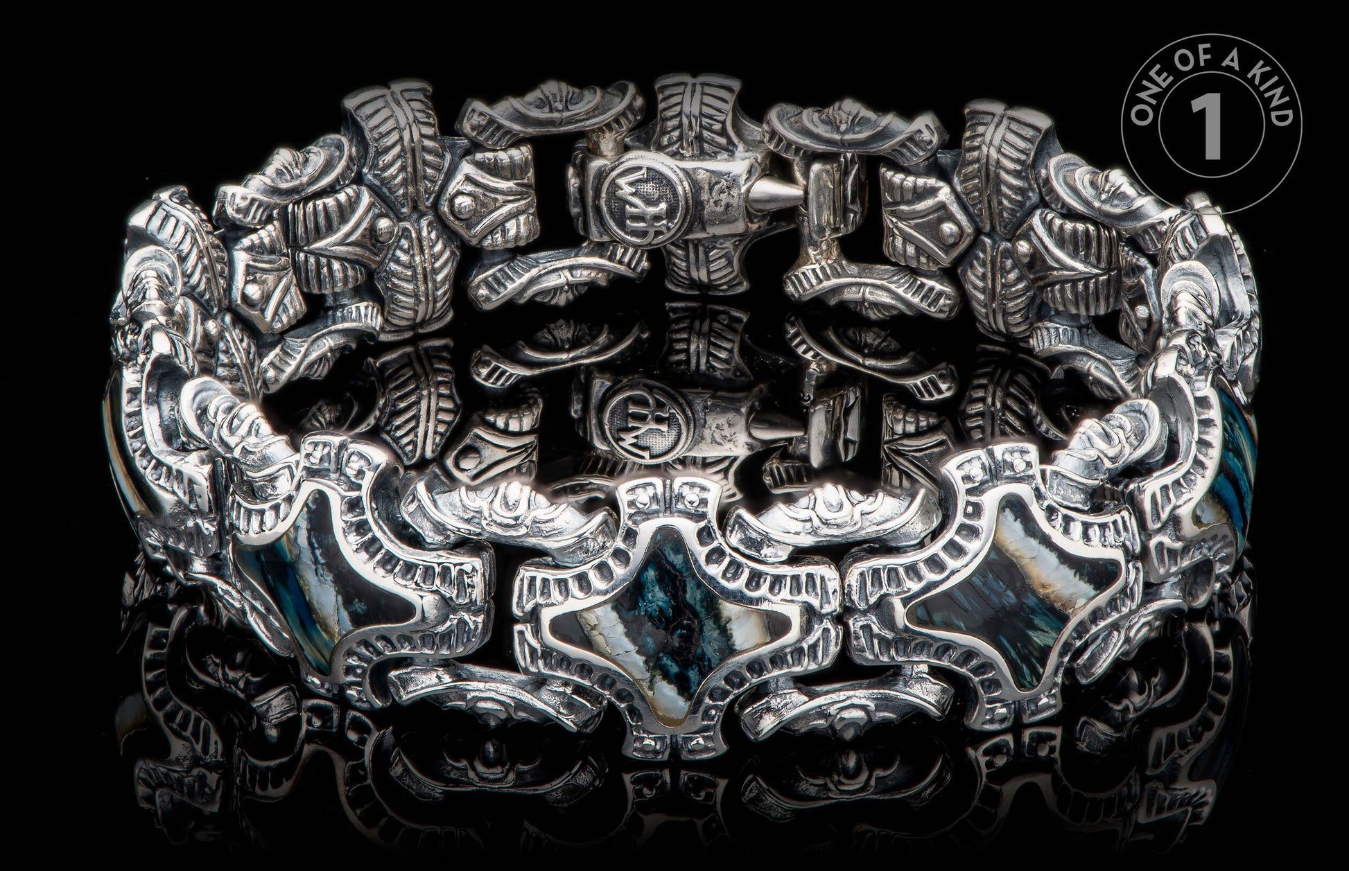 Silver bracelet with intricate carved patterns and dark blue-green shell inlays on a reflective black surface.