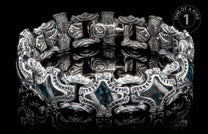 Silver bracelet with intricate carved patterns and dark blue-green shell inlays on a reflective black surface.