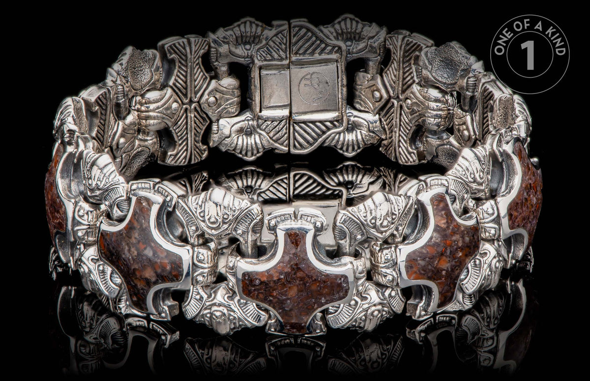 Ornate silver-toned bracelet with dark reddish-brown stone inlays, featuring intricate carved figures and a prominent clasp with "WH" initials.