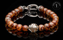 Beaded bracelet with brown and cream eye-patterned stones, a silver-toned clasp, and an ornate silver centerpiece on a reflective black surface.