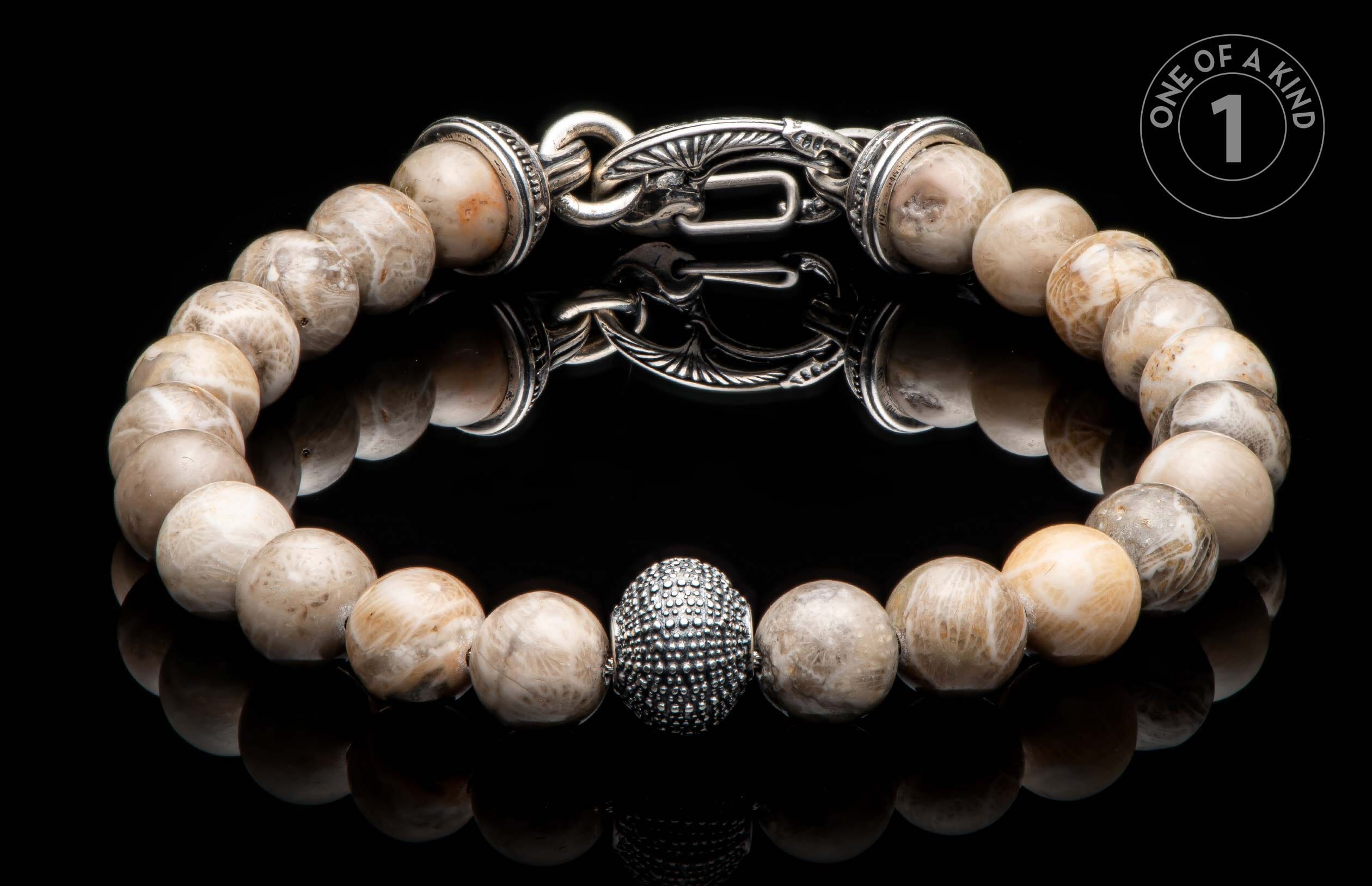 Light-toned natural stone beaded bracelet with an ornate silver clasp, textured oval bead, and "ONE OF A KIND" graphic.