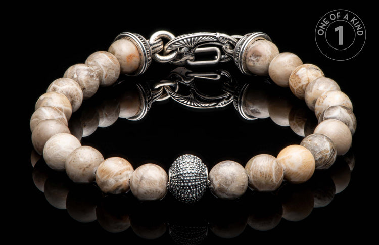 Light-toned natural stone beaded bracelet with an ornate silver clasp, textured oval bead, and "ONE OF A KIND" graphic.