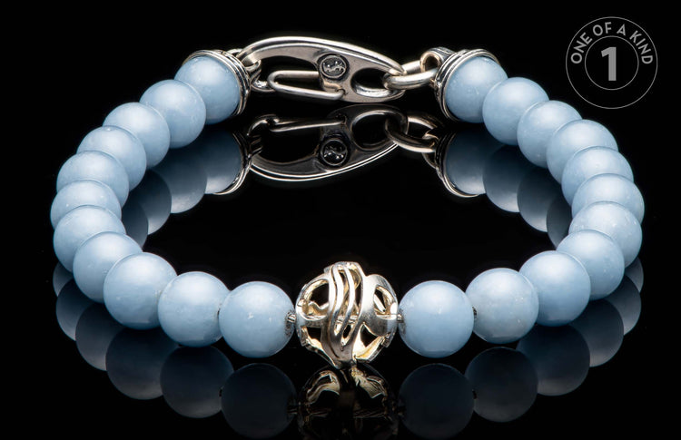 Light blue beaded bracelet featuring a silver-tone ornate clasp and an intricate central charm, reflected on a dark surface.
