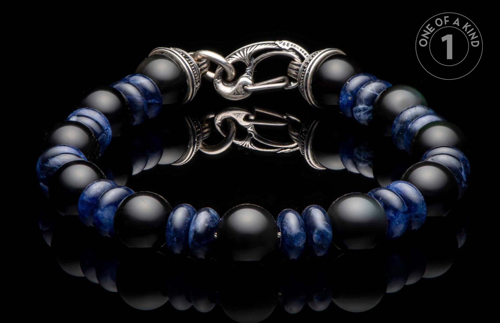 Black matte and blue patterned bead bracelet with an ornate silver clasp on a reflective surface.