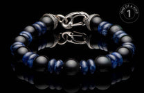 Black matte and blue patterned bead bracelet with an ornate silver clasp on a reflective surface.
