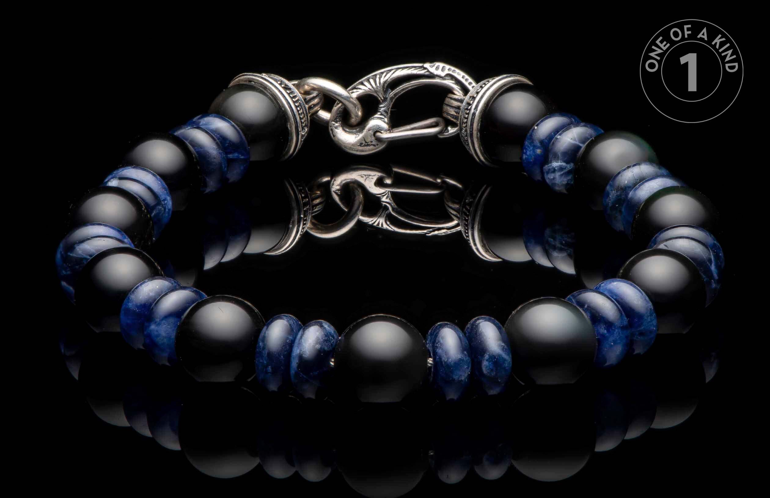 Black matte and blue patterned bead bracelet with an ornate silver clasp on a reflective surface.
