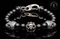 Black onyx beaded bracelet with a silver-toned skull and crossbones charm, two ornate skull beads, and a hook clasp.
