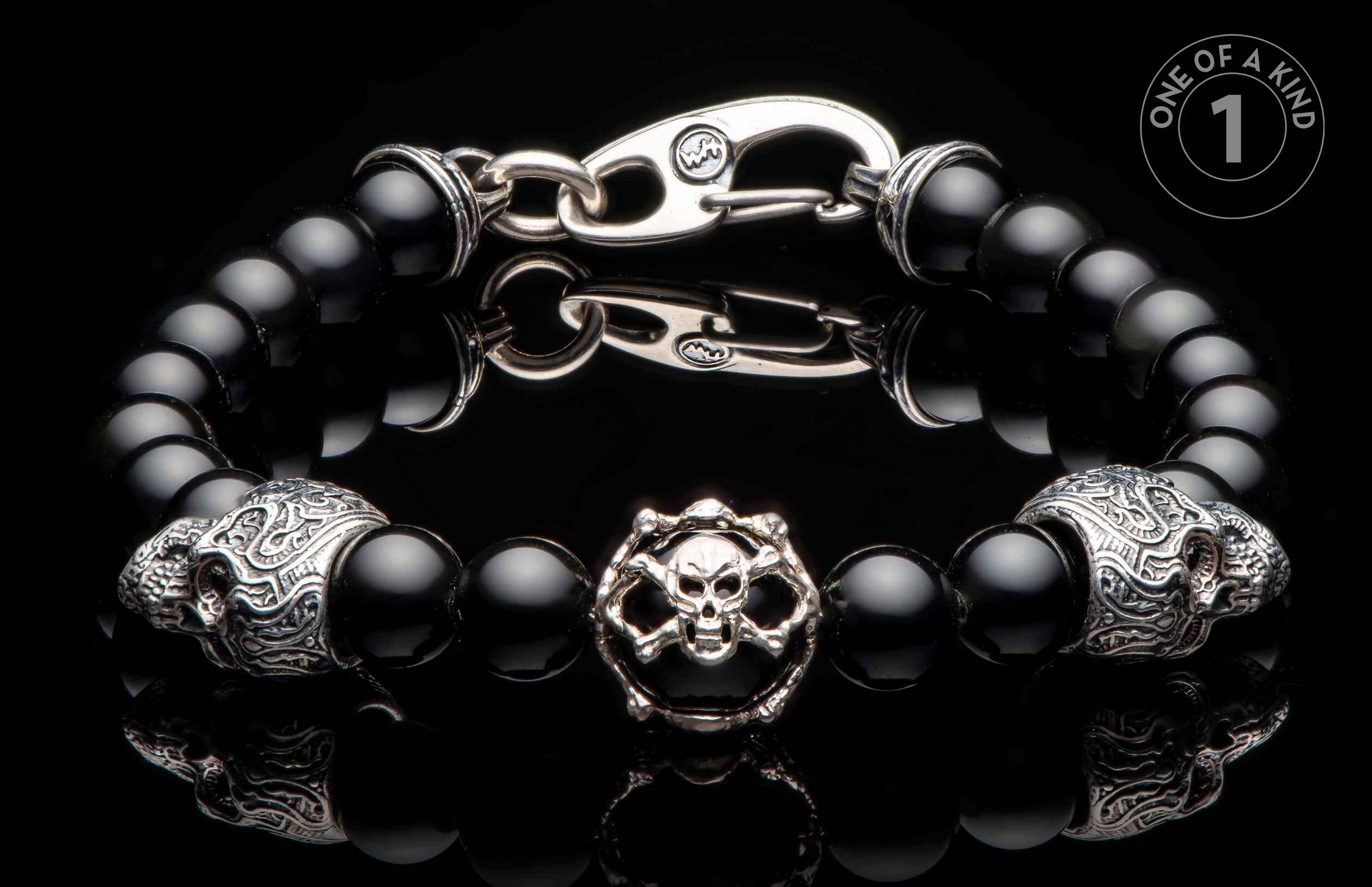 Black onyx beaded bracelet with a silver-toned skull and crossbones charm, two ornate skull beads, and a hook clasp.