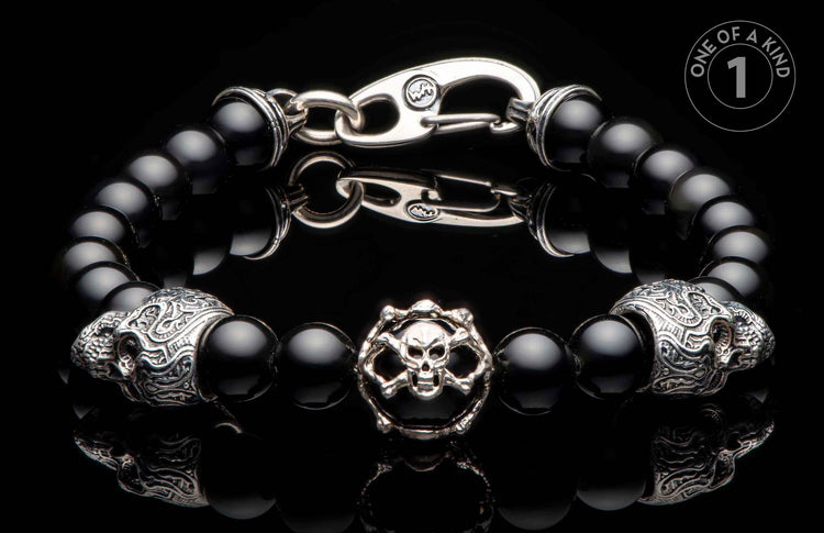 Black onyx beaded bracelet with a silver-toned skull and crossbones charm, two ornate skull beads, and a hook clasp.