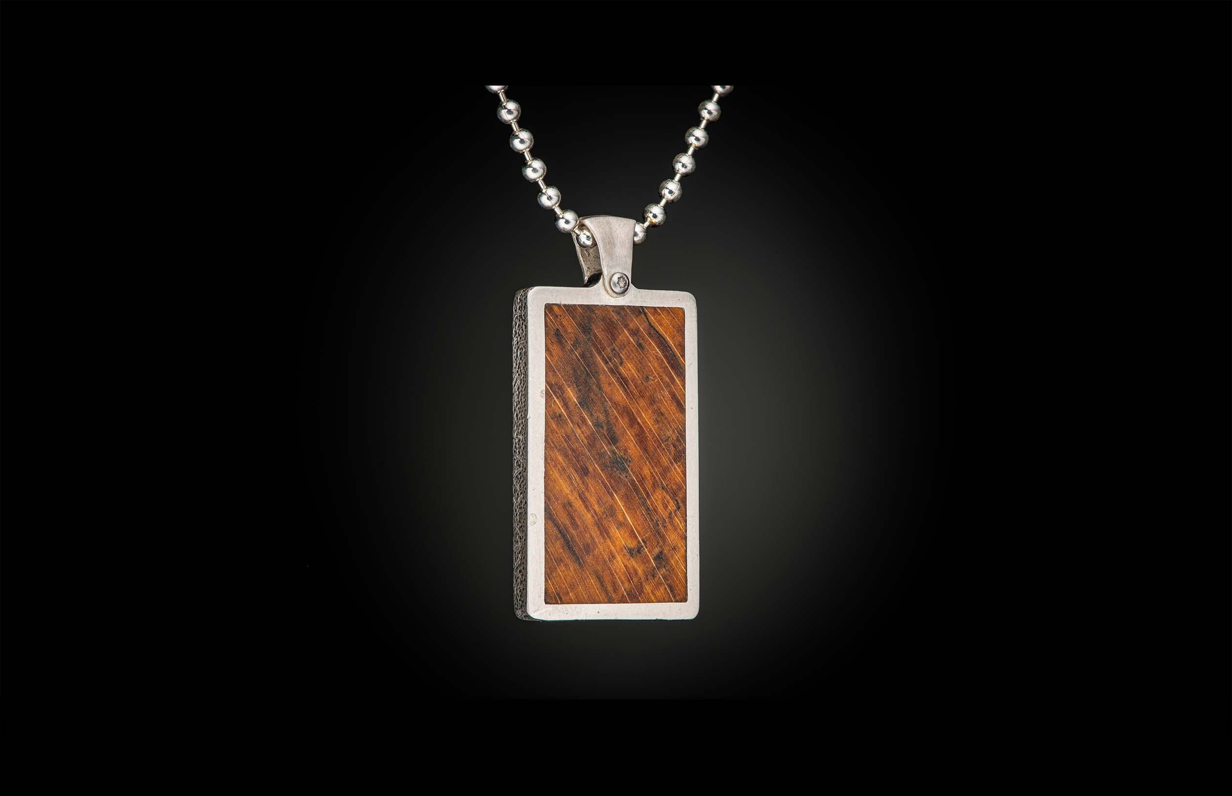 Rectangular pendant with a reddish-brown wood inlay featuring diagonal grain, set in a textured silver-tone metal frame, suspended from a ball chain.