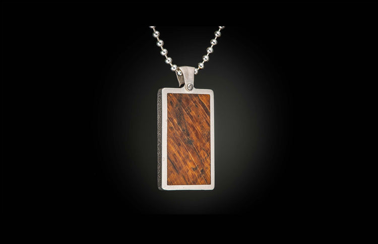 Rectangular pendant with a reddish-brown wood inlay featuring diagonal grain, set in a textured silver-tone metal frame, suspended from a ball chain.