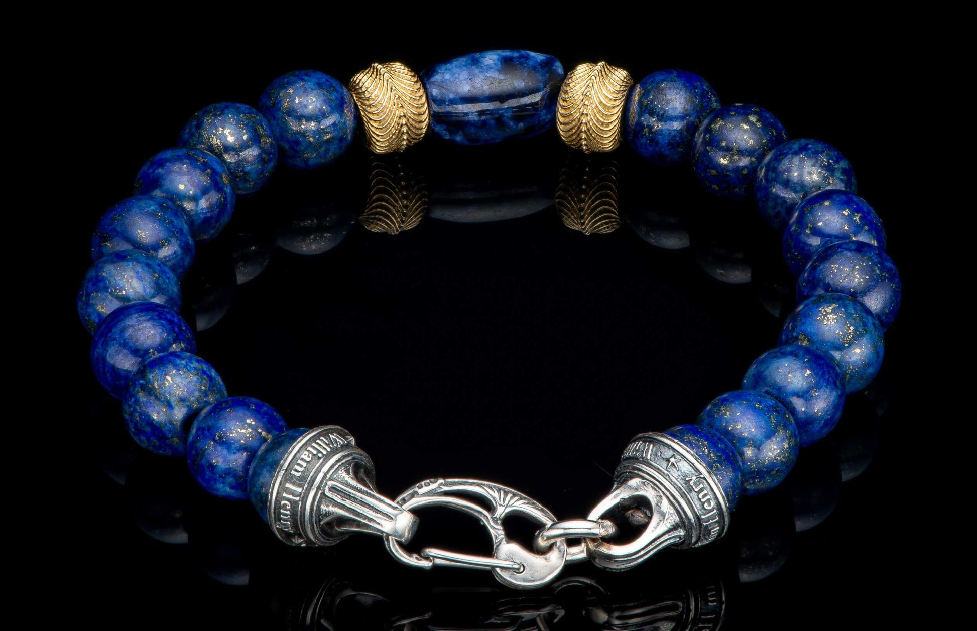Blue lapis lazuli beaded bracelet by William Henry, featuring gold accent beads and a decorative silver clasp on a reflective surface.