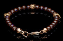 Beaded bracelet with dark brown, iridescent blue-flashing beads and ornate rose gold-toned metal accents, displayed on a reflective black surface.