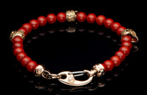 Red beaded bracelet with ornate gold-toned accents and a distinctive hook clasp on a reflective black surface.