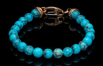 Turquoise beaded bracelet with natural veining and a gold-toned clasp, displayed on a reflective black surface.