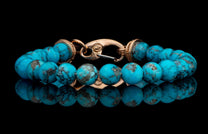 Turquoise beaded bracelet with a rose gold clasp, resting on a reflective black surface.