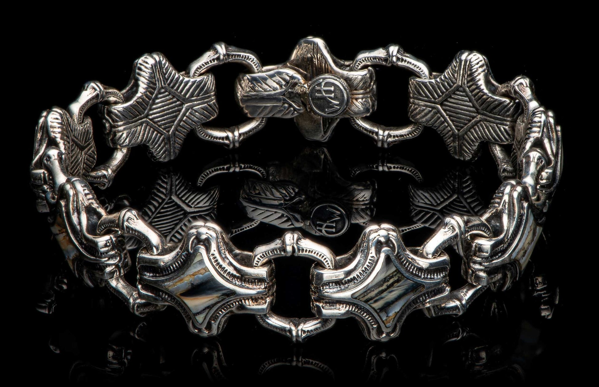 Silver-toned metal bracelet with alternating ornate links, featuring stylized leaf patterns, a 'WH' emblem, and striped inlays.