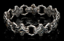Silver-toned metal bracelet with alternating ornate links, featuring stylized leaf patterns, a 'WH' emblem, and striped inlays.