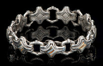 Silver bracelet featuring intricate star-shaped links and rectangular links with striped shell inlay, on a reflective black surface.