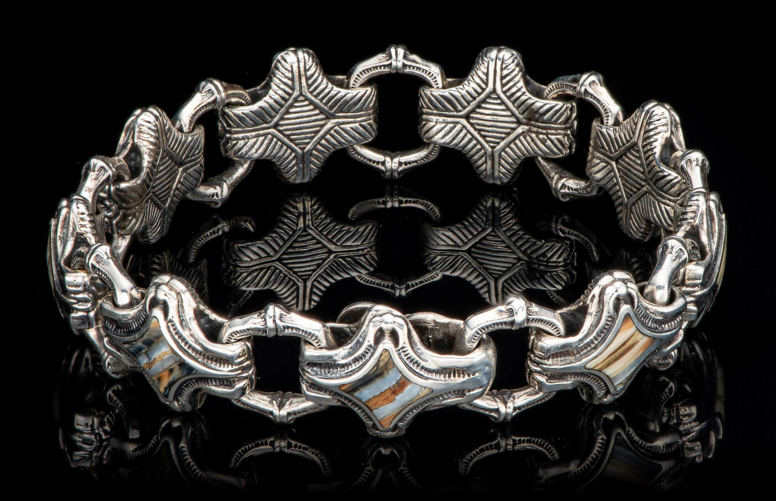 Silver bracelet featuring intricate star-shaped links and rectangular links with striped shell inlay, on a reflective black surface.