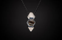 Silver pendant featuring a hexagonal fossilized stone, accented with blue sapphires, suspended on a dark chain.