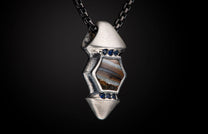Textured silver pendant with a hexagonal brown and white striated stone, accented by six small blue gemstones, on a dark chain.