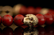 A red beaded bracelet with a textured gold skull bead featuring red gemstone eyes.
