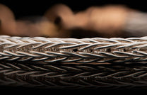 Braided silver-colored chain jewelry with a tightly woven pattern reflecting on a dark surface.