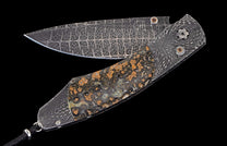 Ornate folding knife with a geometric patterned Damascus blade and a mottled dark stone handle.