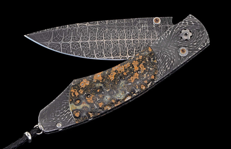 Ornate folding knife with a geometric patterned Damascus blade and a mottled dark stone handle.