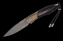 Folding knife with a Damascus steel blade, dark patterned handle with brass sun and star engravings, and braided leather lanyard.