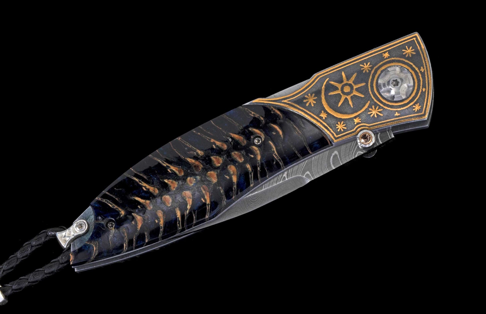 Folding knife with dark handle featuring warm organic patterns, decorative bolster with gold sun and star engravings, and a Damascus steel blade.