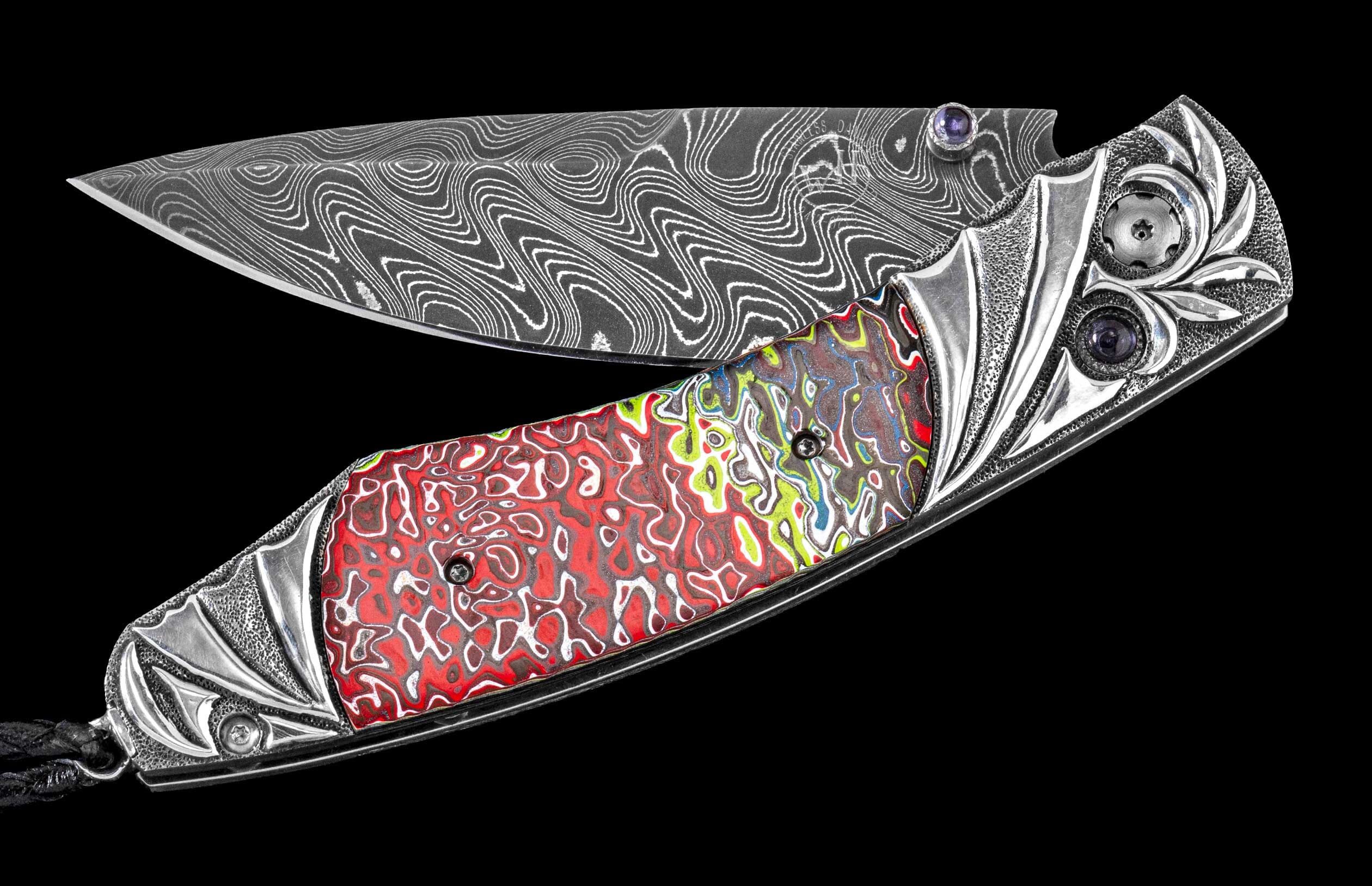 Folding knife with a wavy Damascus steel blade, a colorful abstract handle, and silver-toned carved metal bolsters with purple gems.