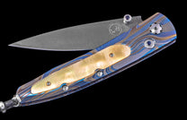 Partially open folding knife with a Damascus blade, a blue and gold swirled handle, cream mother-of-pearl inlay, and blue gem accents.