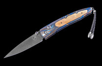 Folding knife with a blue and brown patterned handle, Damascus steel blade, mother-of-pearl inlay, blue jeweled accents, and a braided leather lanyard.