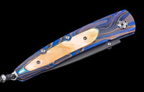 Folding knife with a blue, silver, and gold wavy patterned metal handle, a cream inlay, and a lanyard.