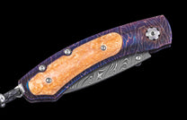 Folded knife with marbled orange handle inserts, a purple patterned frame, Damascus blade, and a braided black lanyard.
