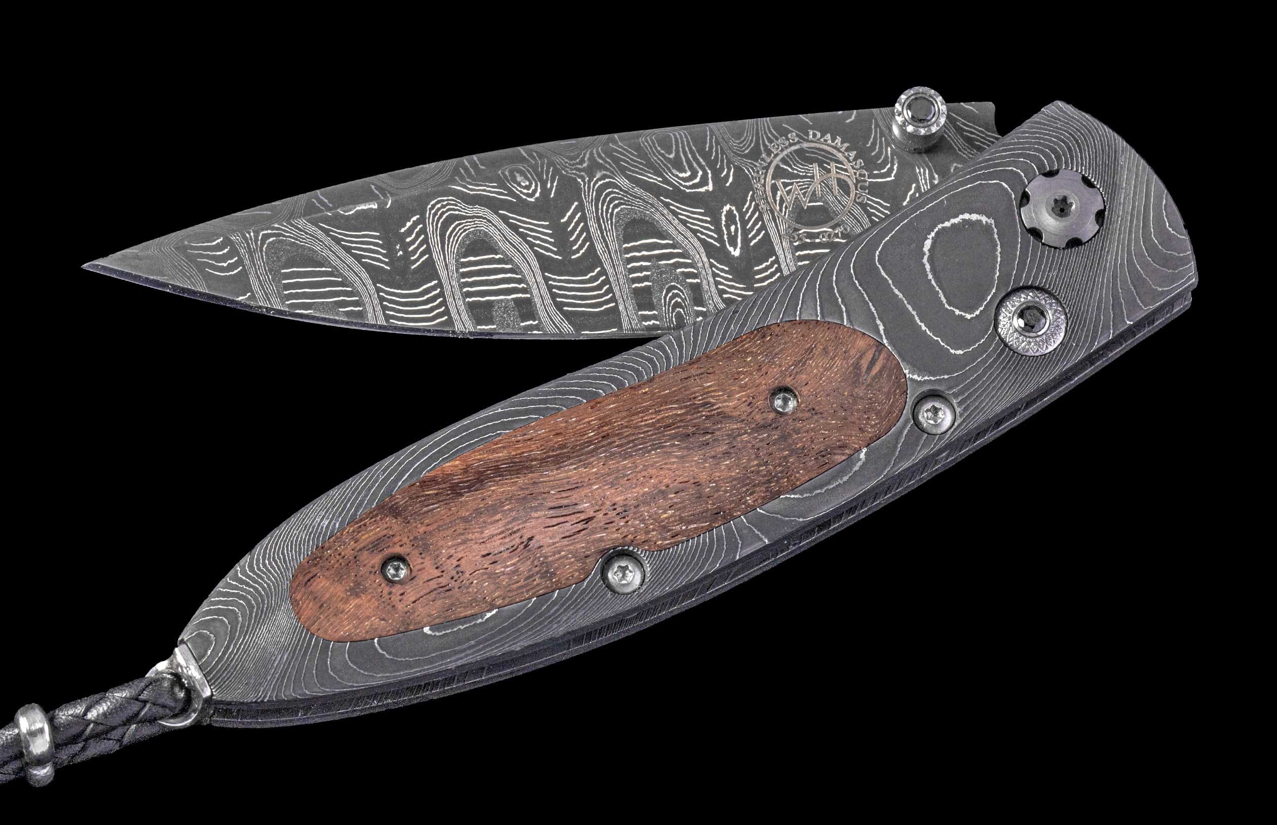 Damascus steel folding knife with a distinctive wavy pattern, featuring a reddish-brown wooden handle inlay and a braided leather lanyard.