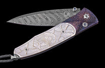 Folding knife with patterned Damascus blade, carved mother-of-pearl handle, textured purple scale, and blue gemstones.