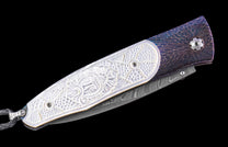 Folding knife with white carved handle, purple and bronze patterned frame, Damascus steel blade, and braided lanyard.
