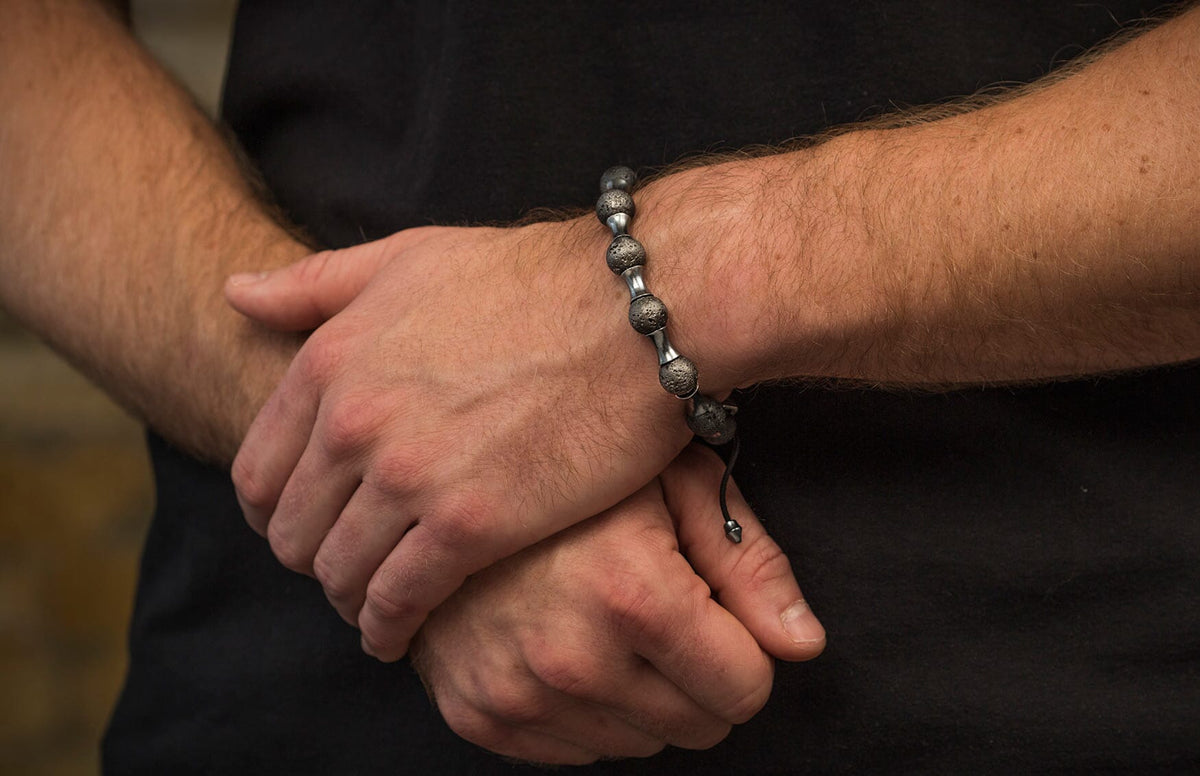 Textured lava bead and silver-toned spacer bracelet with black cord on a man's wrist.