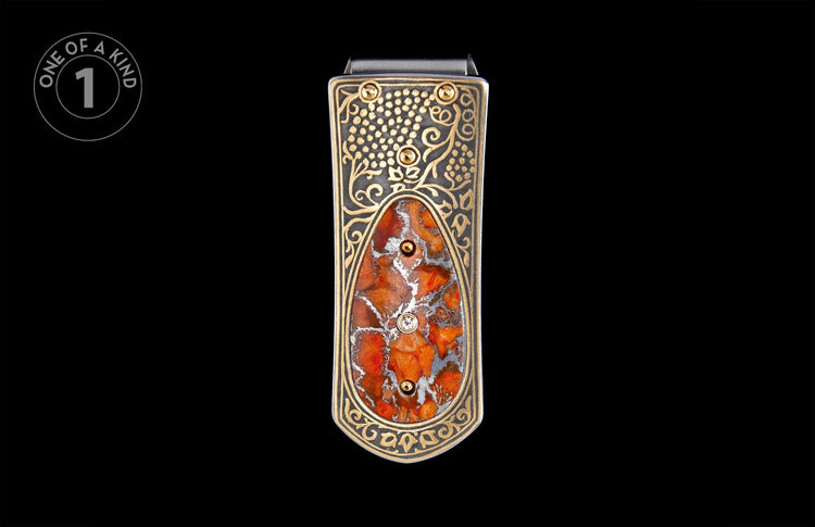 Ornate gold and dark silver money clip with a mottled orange-red stone inlay, accented by gold dots and a clear gemstone.