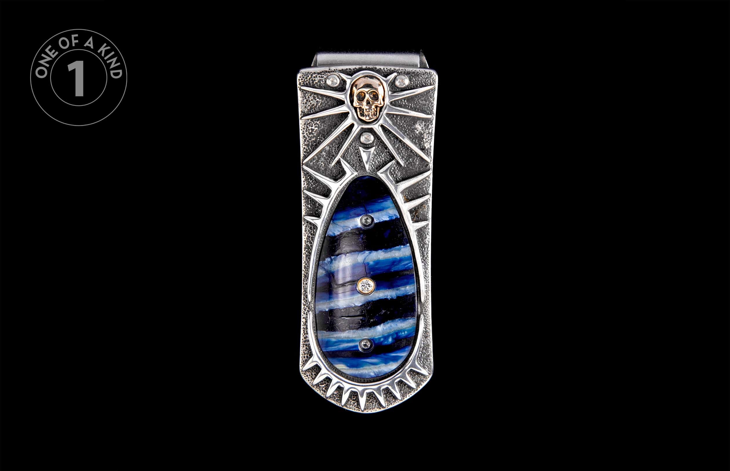 Textured silver money clip with a golden skull, sunburst design, and blue, black, and white striped inlay.