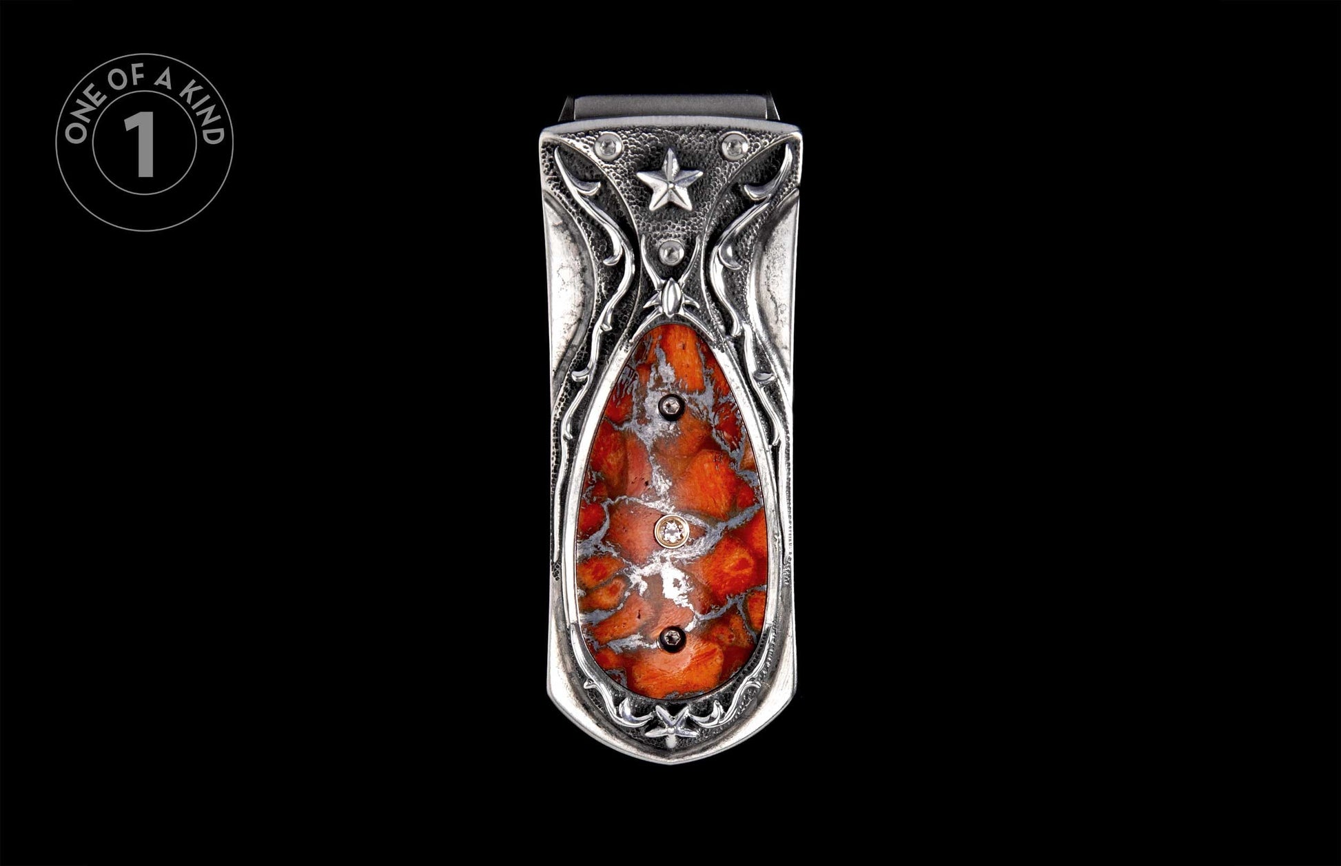 Ornate silver-toned money clip with a central mottled orange and grey stone, featuring scrollwork and a star emblem.